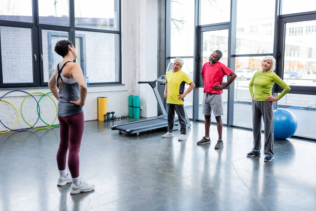 Starší multietničtí lidé cvičení v blízkosti trenéra v tělocvičně  - Fotografie, Obrázek