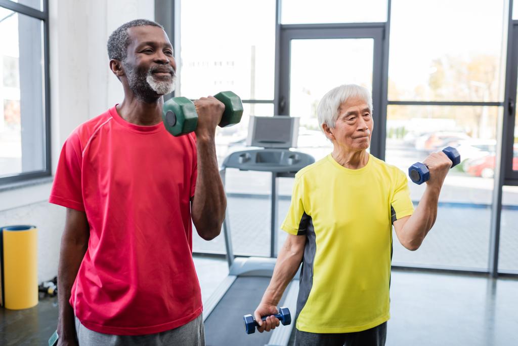 Starsi sportowcy międzyrasowi ćwiczą z hantlami na siłowni  - Zdjęcie, obraz