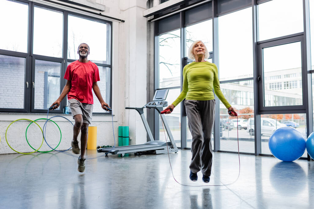 Sonriendo gente interracial entrenando con cuerdas de salto en el gimnasio  - Foto, Imagen