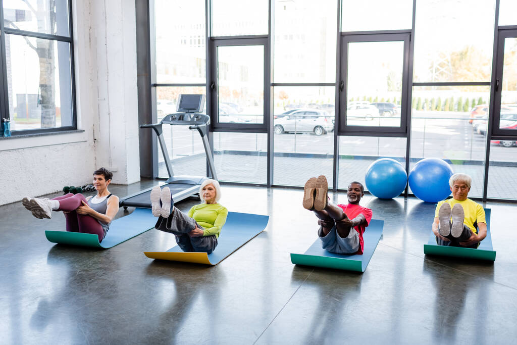 Мультикультурные люди в спортивной одежде тренируются на фитнес-ковриках в спортзале  - Фото, изображение