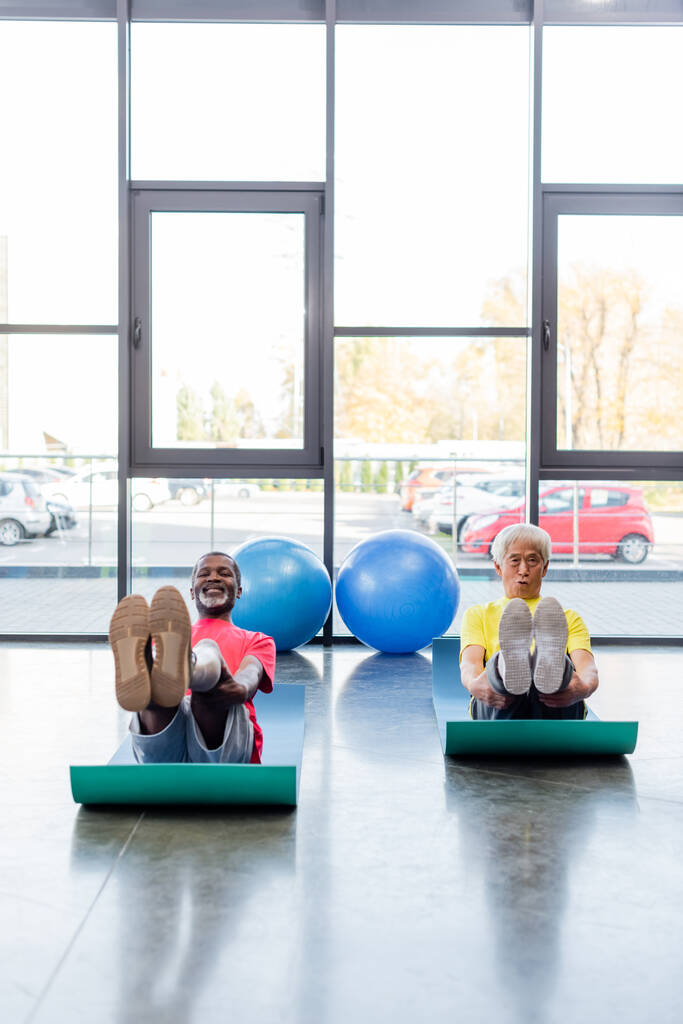 Des sportifs multiethniques souriants s'entraînent sur des tapis de fitness dans une salle de sport  - Photo, image