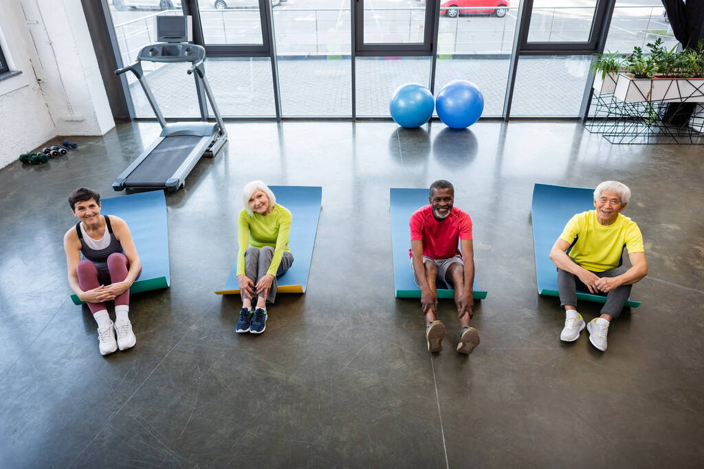Vysoký úhel pohledu na multietnické seniory sedící na fitness podložky v tělocvičně - Fotografie, Obrázek