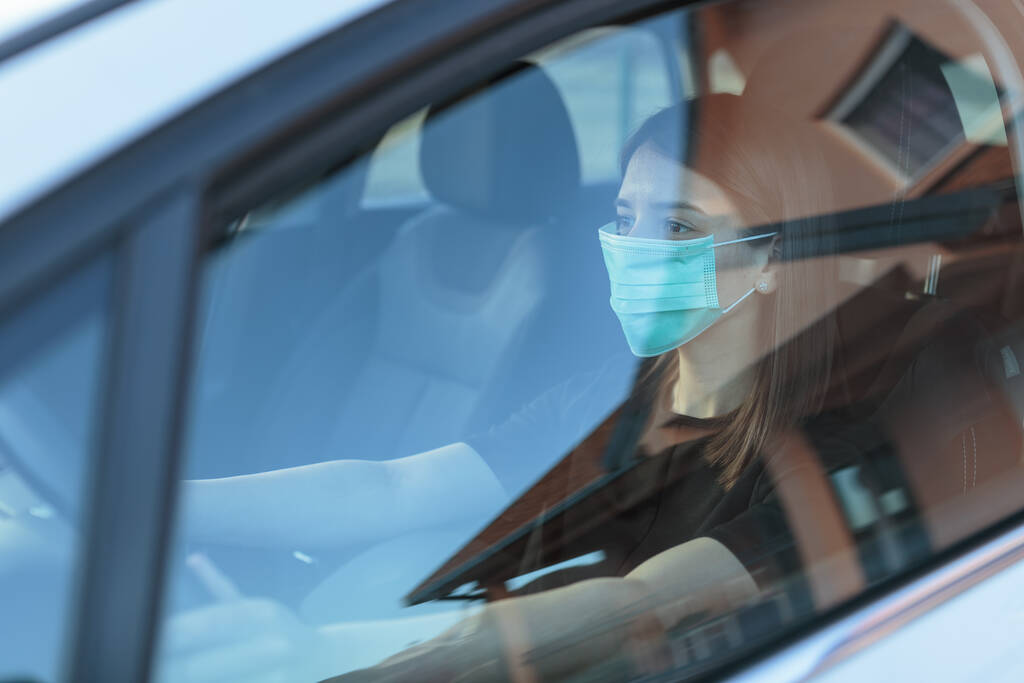 Eine Kaukasierin mit Gesichtsmaske am Steuer eines Autos - Foto, Bild