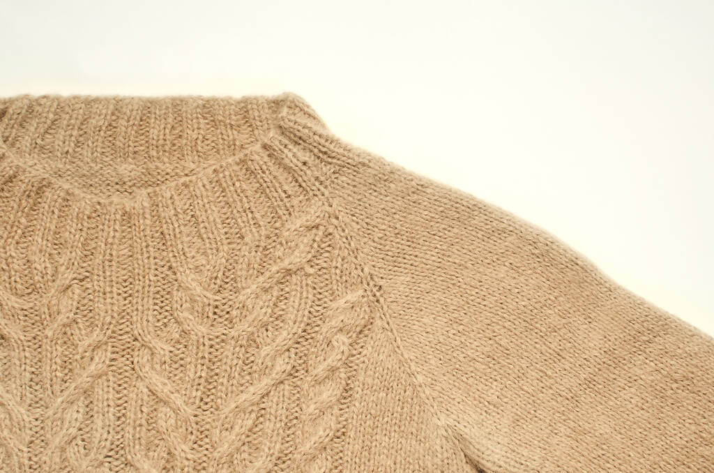 Fragment van een beige gebreide trui met een patroon op een witte achtergrond. Halsband, close-up. - Foto, afbeelding