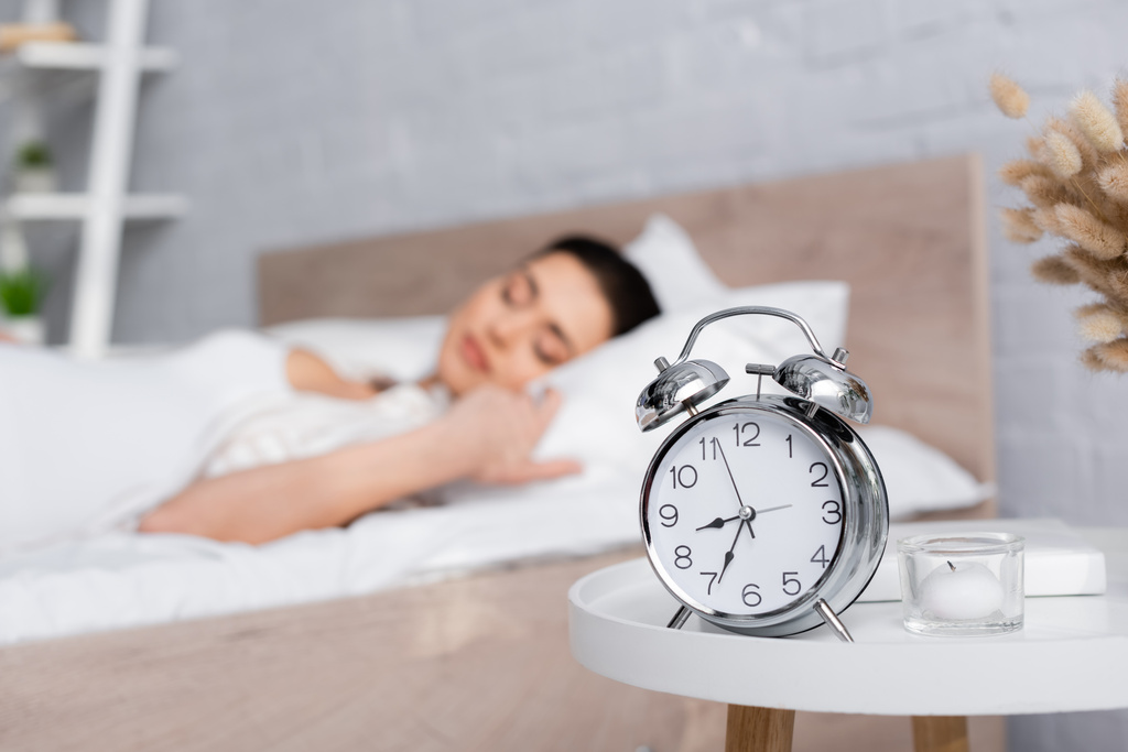 Retro-Wecker auf Couchtisch neben verschwommener schlafender Frau - Foto, Bild