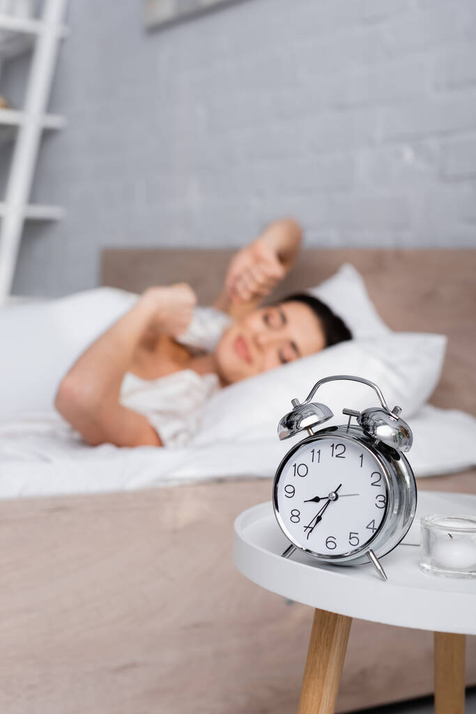 ретро будильник на кавовому столі біля розмитої сонної жінки
 - Фото, зображення