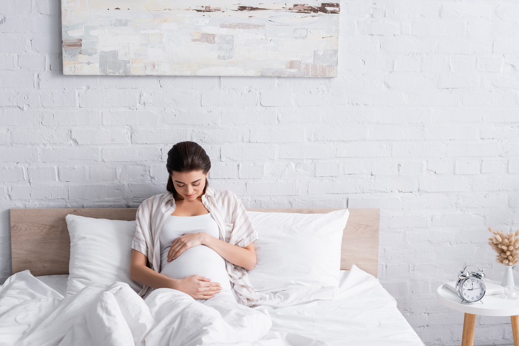 potěšen a těhotná mladá žena dotýká břicho v ložnici - Fotografie, Obrázek