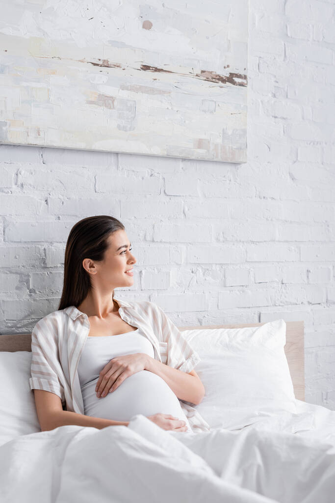 Glückliche Schwangere schaut im Schlafzimmer weg  - Foto, Bild