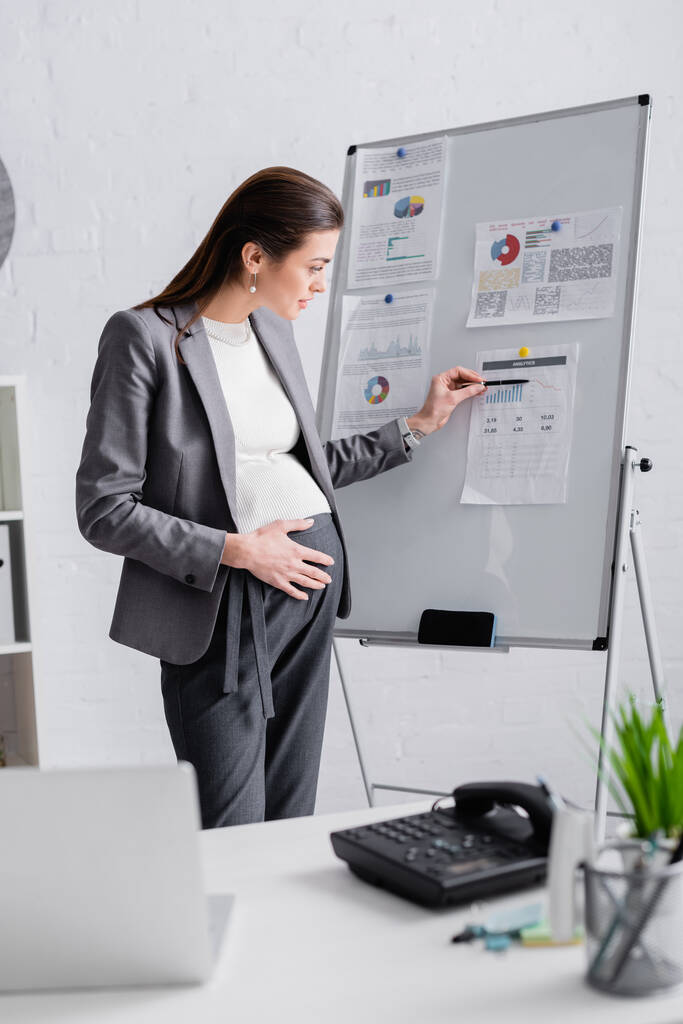 terhes nő mutat flip chart közelében elmosódott laptop az asztalon  - Fotó, kép