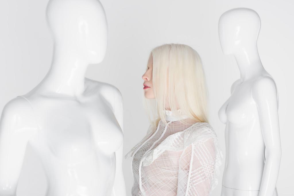 Боковой вид женщины-альбиноса в блузке, стоящей рядом с манекенами, изолированными на белом  - Фото, изображение