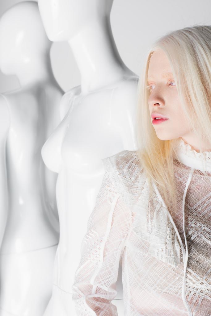 Mooie albino vrouw in blouse staan in de buurt van mannequins geïsoleerd op wit  - Foto, afbeelding