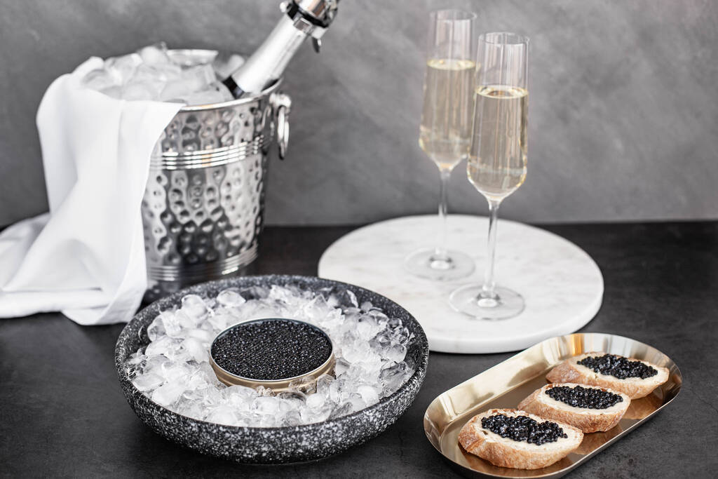 Zwarte kaviaar in blik op ijs, kaviaar sandwich op gouden bord, champagne in glas - Foto, afbeelding