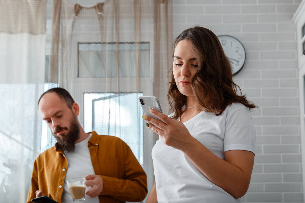 Sad Angry young married couple after conflict fight ignoring each other at home interior. Angry fury woman use smartphone. Man has phone addiction. - Photo, Image