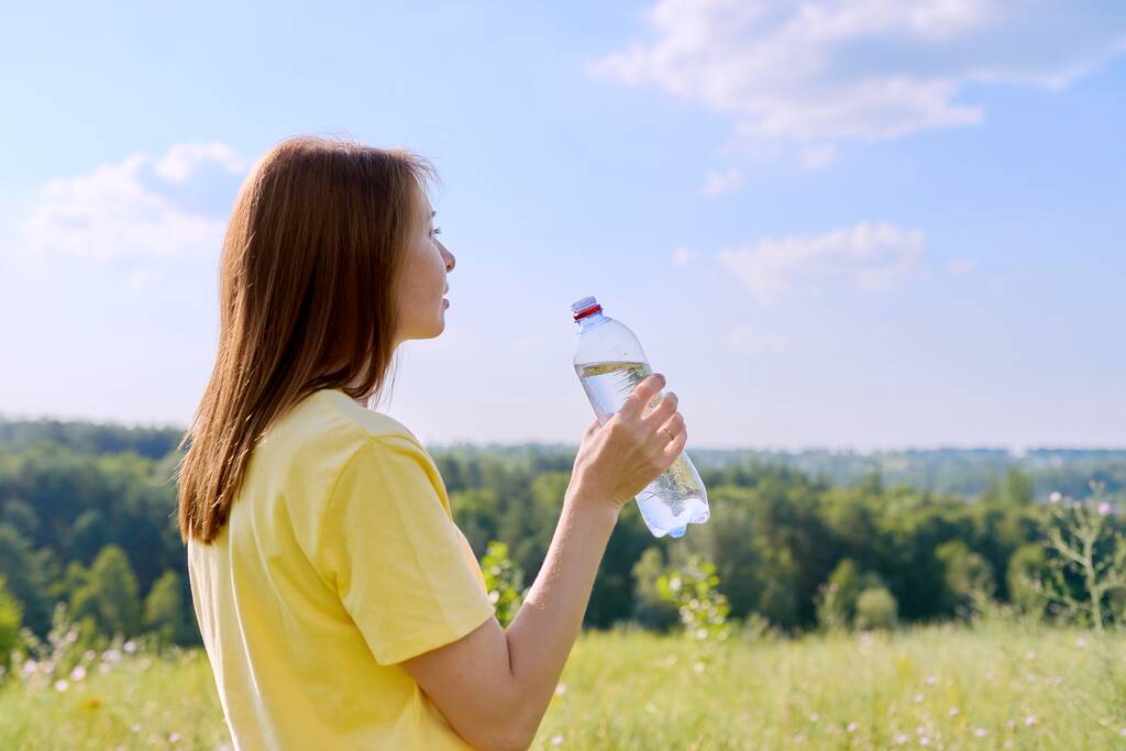 暑い夏、喉が渇いた大人の女性は自然の中で私たちにボトルから水を飲む - 写真・画像