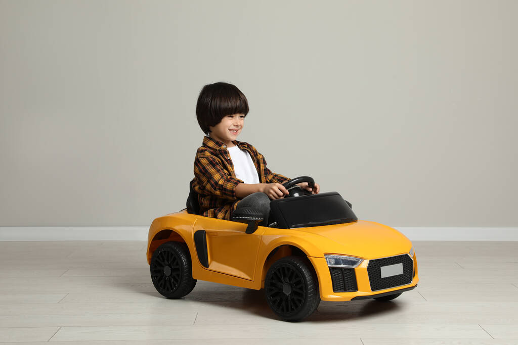 Schattig jongetje rijden kinderen elektrische speelgoed auto in de buurt van grijze muur binnen - Foto, afbeelding