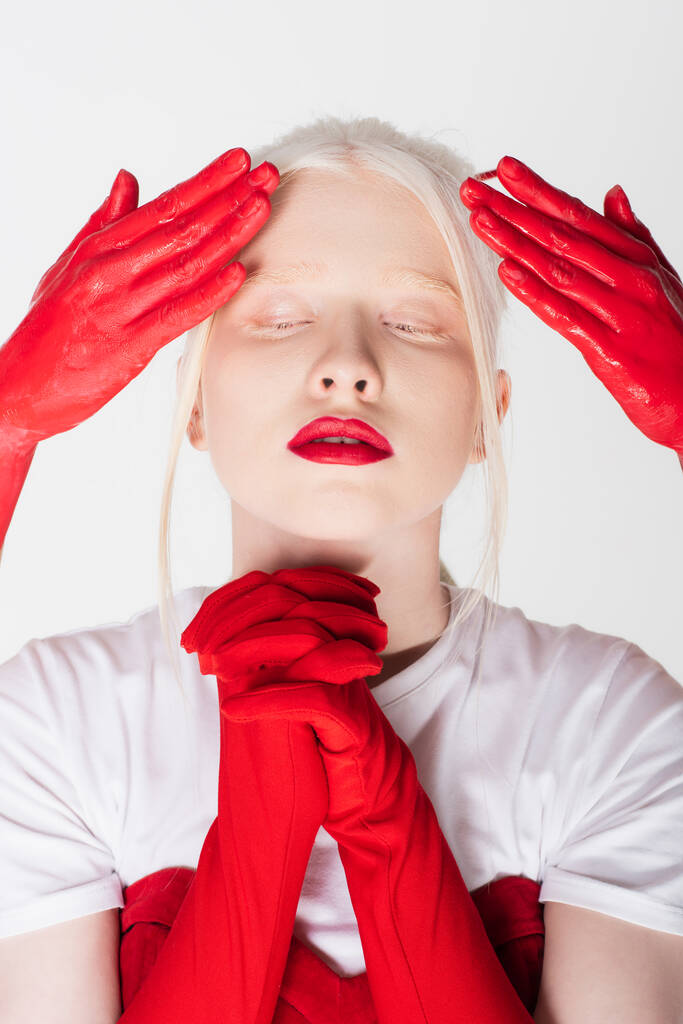 Albínský model s červenými rty stojící poblíž ženských rukou v barvě izolované na bílém - Fotografie, Obrázek
