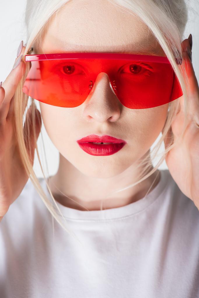 Porträt einer Albino-Frau mit roter Sonnenbrille und Lippen, die isoliert auf weiß in die Kamera blickt - Foto, Bild