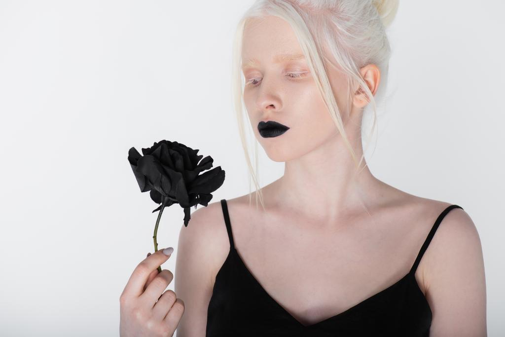 Pretty young albino woman with black lips looking at rose isolated on white - Photo, Image
