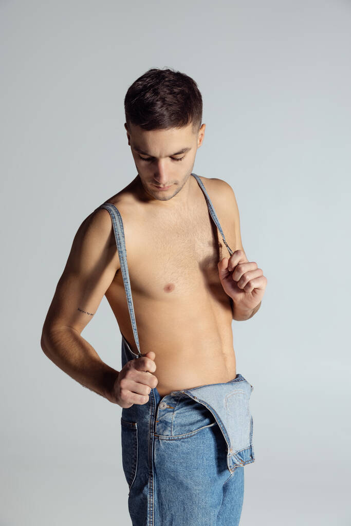 Retrato de un joven guapo y deportivo hombre sin camisa en jeans posando aislado sobre fondo gris del estudio. - Foto, Imagen