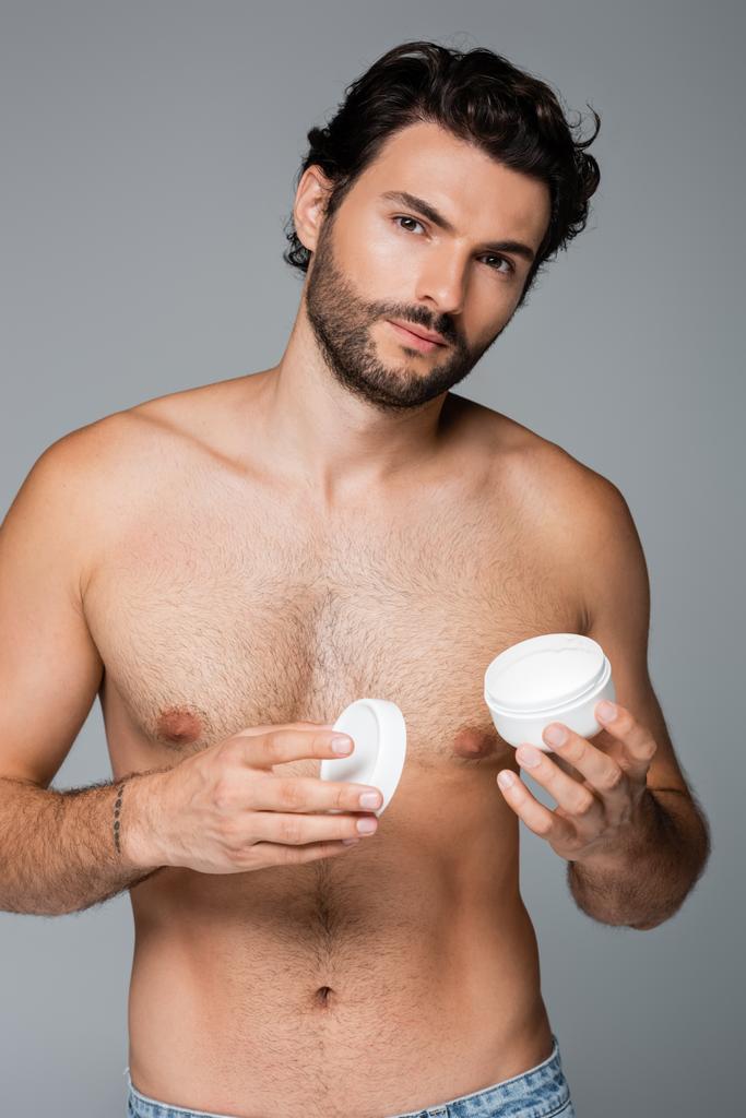 Tätowierter Mann hält Behälter mit Kosmetikcreme isoliert auf grau  - Foto, Bild