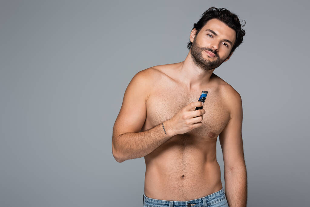 jonge shirtloze man met elektrisch scheermes geïsoleerd op grijs - Foto, afbeelding
