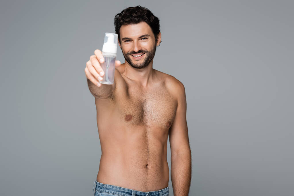 radostný a bez košile muž držící pěnový čistič izolovaný na šedé - Fotografie, Obrázek