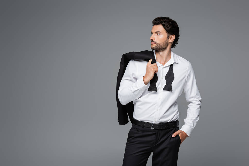 бородатий чоловік у костюмі тримає блістер і стоїть з рукою в кишені ізольовано на сірому
 - Фото, зображення
