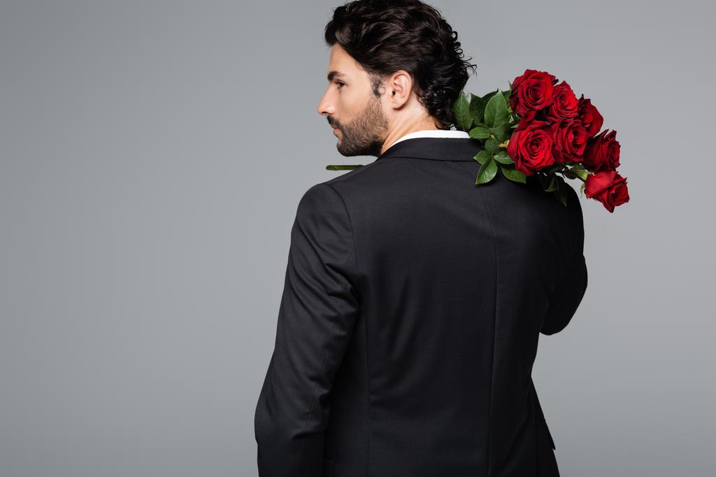 γενειοφόρος άνδρας με κοστούμι κρατώντας μπουκέτο από κόκκινα τριαντάφυλλα που απομονώνονται σε γκρι - Φωτογραφία, εικόνα