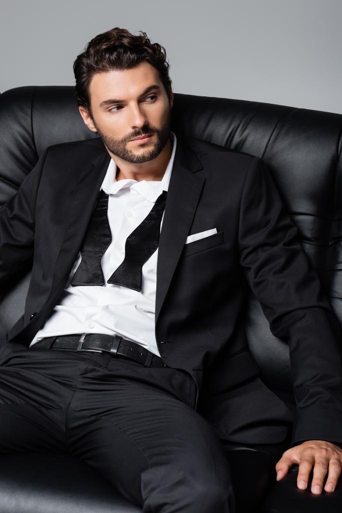bearded man in formal wear sitting on black couch isolated on grey - Photo, Image