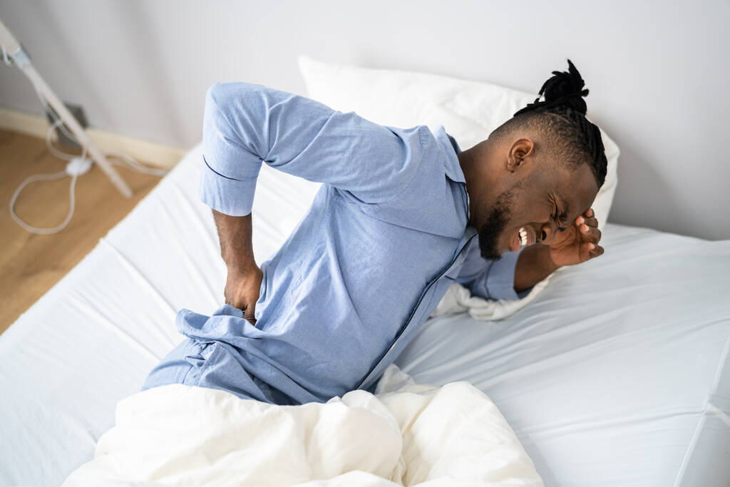 Mężczyzna cierpiący na ból pleców siedzi na łóżku - Zdjęcie, obraz
