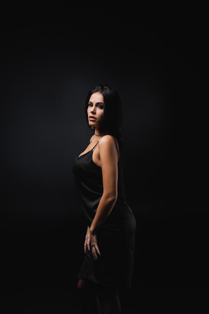 brunette jonge vrouw in slip jurk staande geïsoleerd op zwart  - Foto, afbeelding