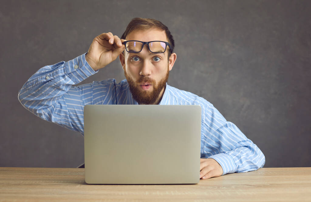Здивований працівник знімає окуляри і дивиться на те, що шокуюче відбувається в офісі
 - Фото, зображення