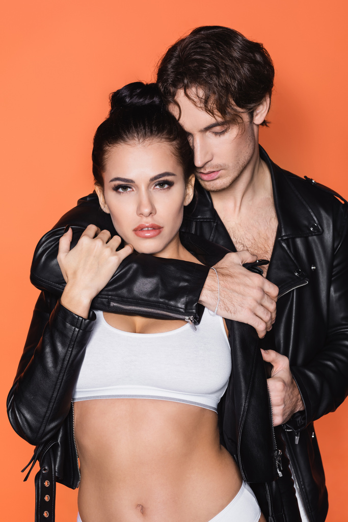 man hugging young woman in black leather jacket isolated on orange - Photo, Image
