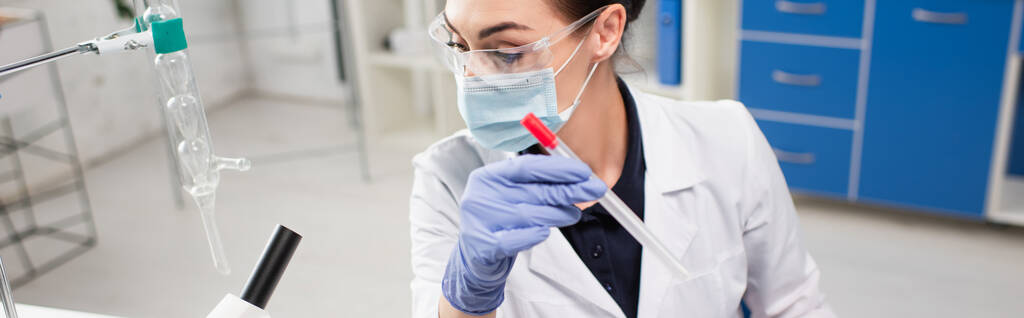 Ученый в медицинской маске проводит тест pcr возле микроскопа в лаборатории, баннер  - Фото, изображение