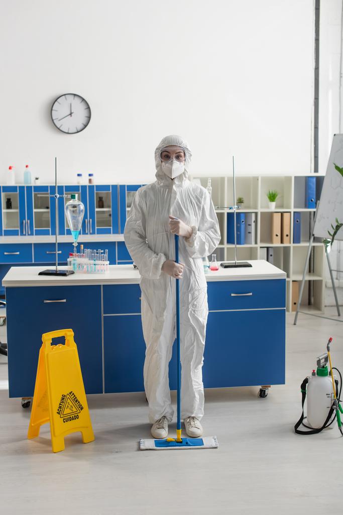 naukowiec w kombinezonie ochronnym i goglach trzymający mop podczas czyszczenia laboratorium - Zdjęcie, obraz