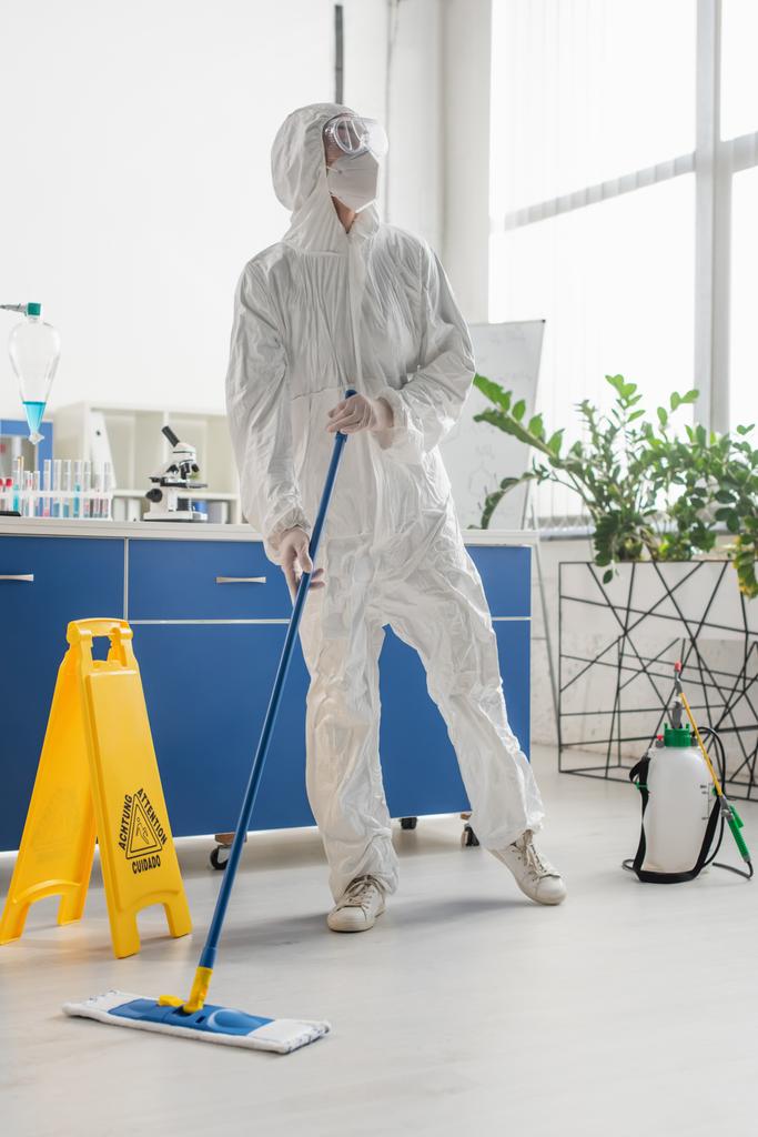 scienziato in tuta hazmat distogliendo lo sguardo mentre pulisce il pavimento in laboratorio - Foto, immagini