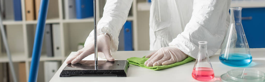 обрезанный вид врача протирающего стол в лаборатории рядом с фляжками и чашками Петри, баннер - Фото, изображение