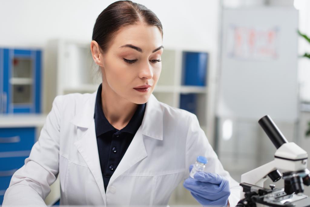 brunette wetenschapper in witte vacht met coronavirus vaccin in laboratorium - Foto, afbeelding