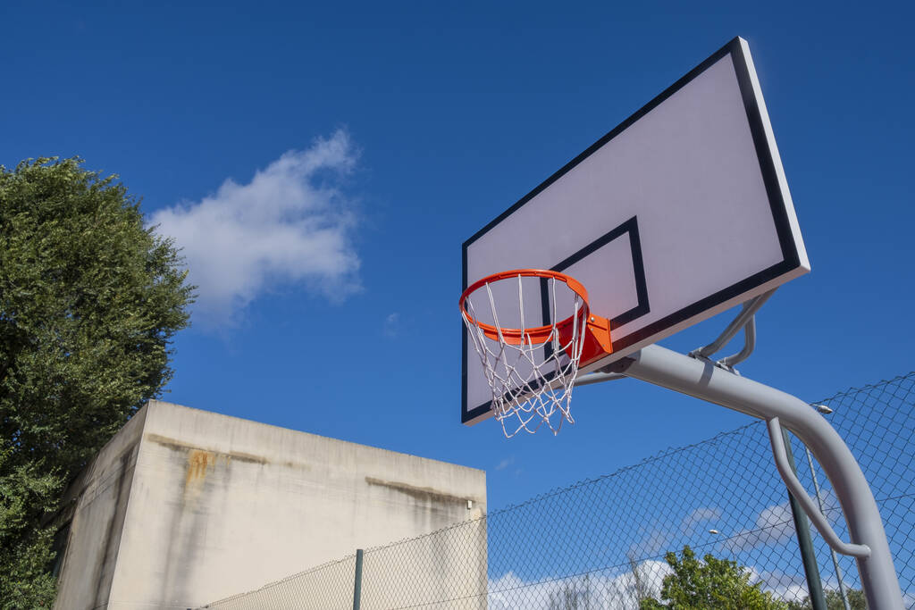 Μια χαμηλή γωνία ενός δακτυλίου μπάσκετ ενάντια στο συννεφιασμένο ουρανό - Φωτογραφία, εικόνα
