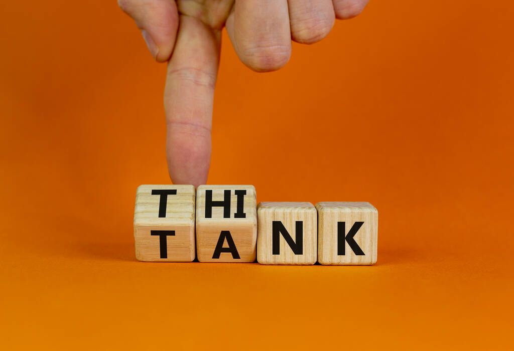 Pomyśl o symbolu czołgu. Biznesmen zamienia drewniane kostki i zmienia słowo "czołg" na "myśleć" lub odwrotnie. Piękny pomarańczowy stół, pomarańczowe tło, przestrzeń do kopiowania. Biznes, koncepcja think tanku. - Zdjęcie, obraz