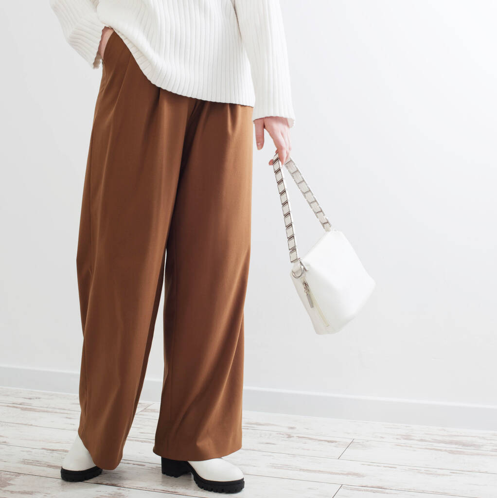 chica moderna en suéter blanco y pantalones marrones en habitación blanca - Foto, Imagen