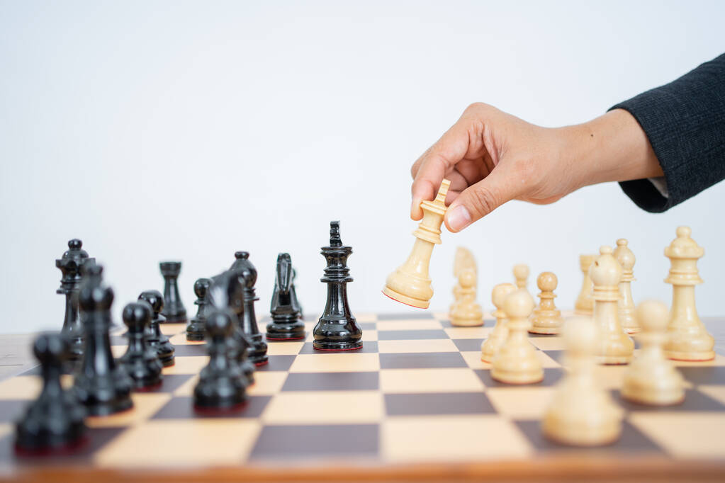 Χέρι κρατώντας το βασιλιά για να επιτεθεί, ενώ παίζει σκάκι στη σκακιέρα - Φωτογραφία, εικόνα