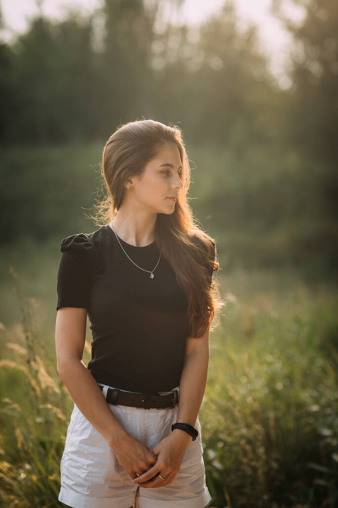 Uma jovem beleza caminha sob os raios do sol de verão nos prados da vegetação rasteira. - Foto, Imagem
