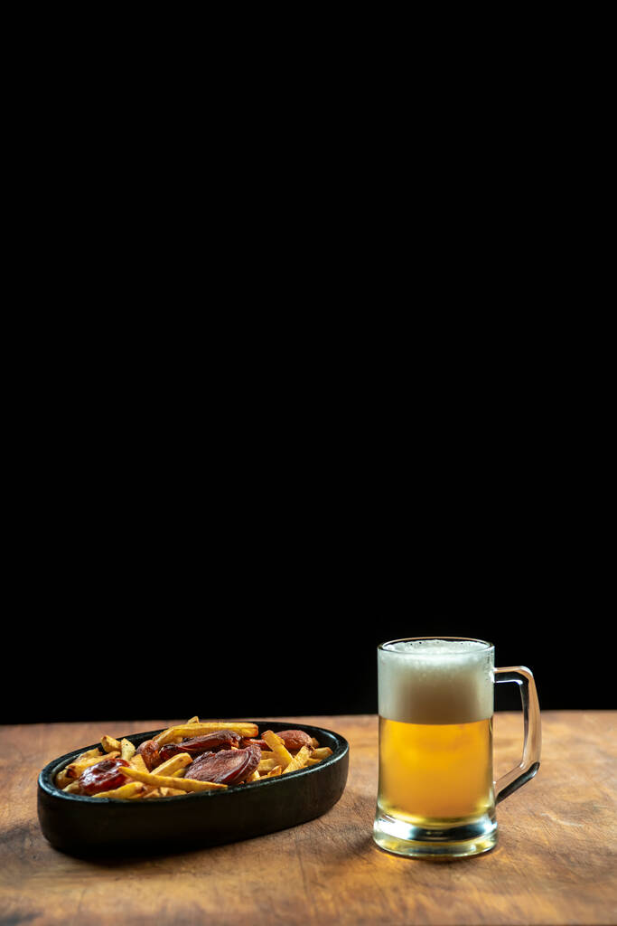 espuma en un vaso con cerveza y salchichas fritas con patatas sobre un fondo de madera.Oktoberfest. - Foto, Imagen