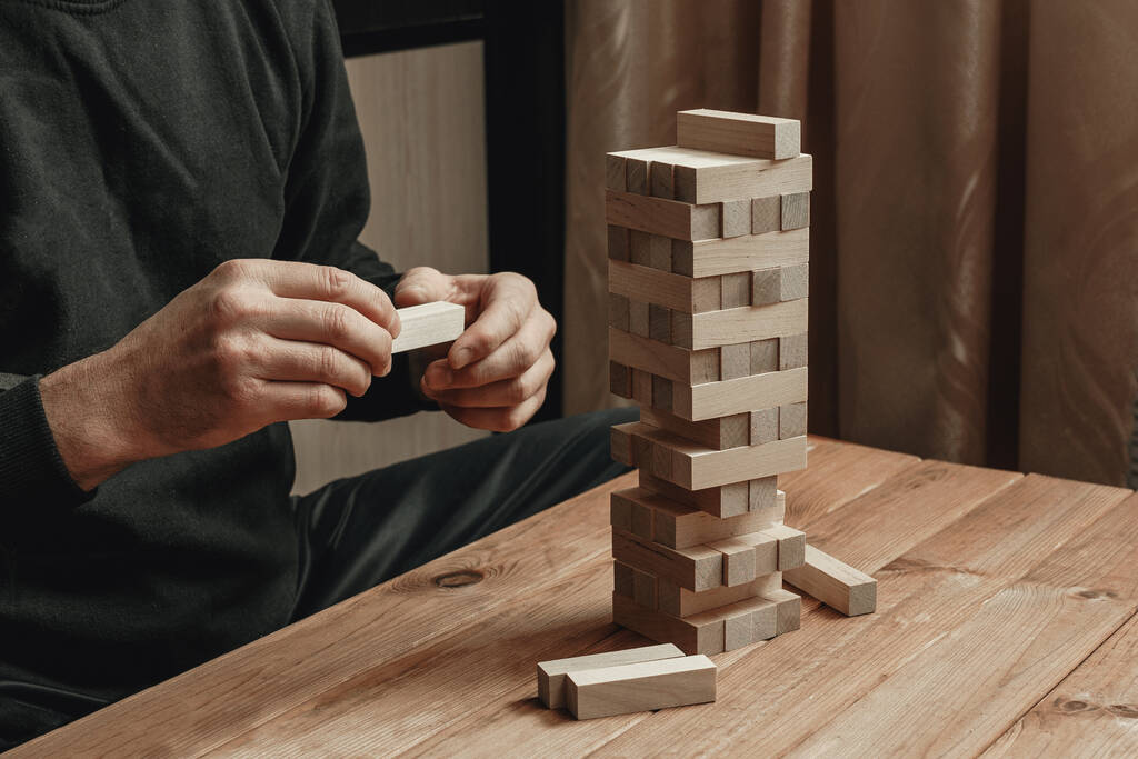 Τα χέρια ενός άντρα που παίζει επιτραπέζιο παιχνίδι χτίζουν έναν πύργο από ξύλινα τουβλάκια. - Φωτογραφία, εικόνα