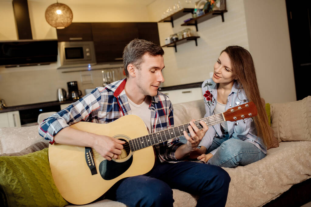 Młody mężczyzna gra na gitarze w domu, a kobieta go słucha i śpiewa - Zdjęcie, obraz