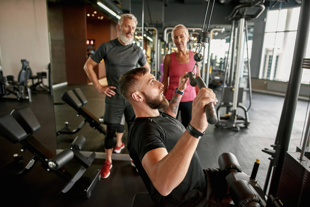 Atletische trainer demonstreert hoe power lifting fitnessapparatuur te gebruiken - Foto, afbeelding