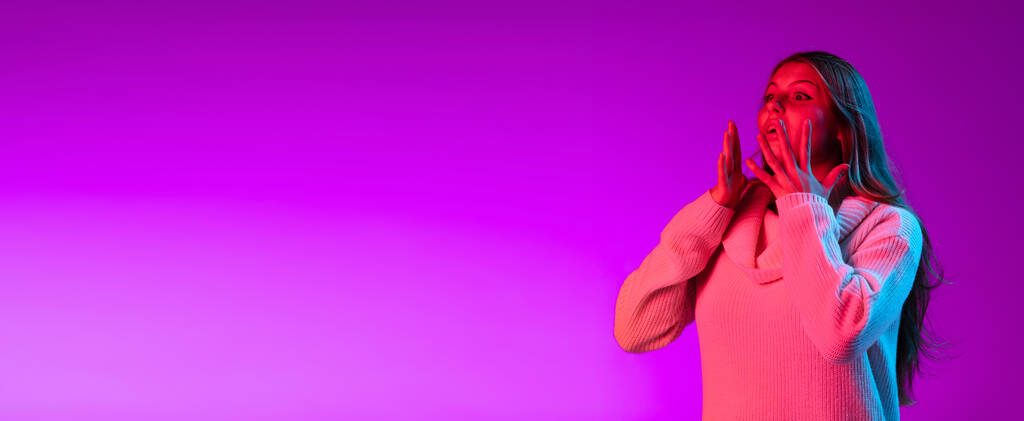 Volantino con ritratto di giovane bella ragazza con lentiggini carino in maglione bianco isolato su sfondo viola studio colore in luce al neon. - Foto, immagini