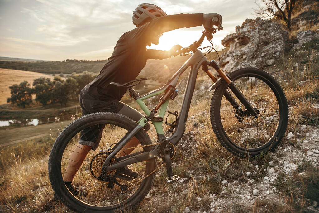 若い男性サイクリストローリングバイクで草の多い山の斜面に日没 - 写真・画像