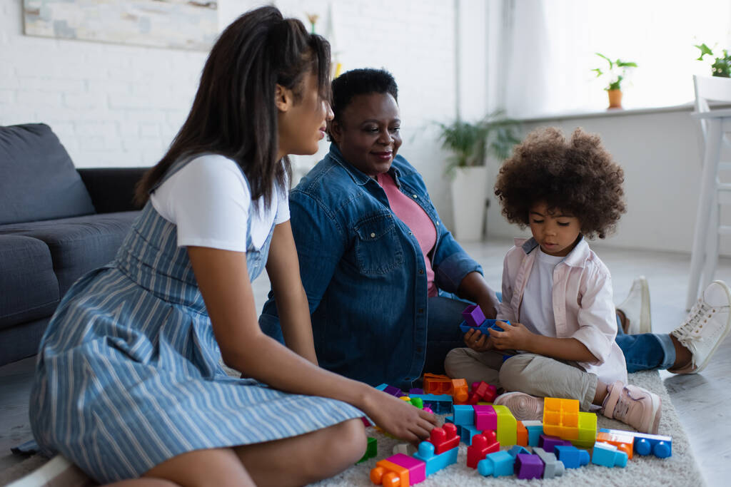 ricci africano americano ragazza giocare con i blocchi di costruzione vicino madre e nonna al piano a casa - Foto, immagini